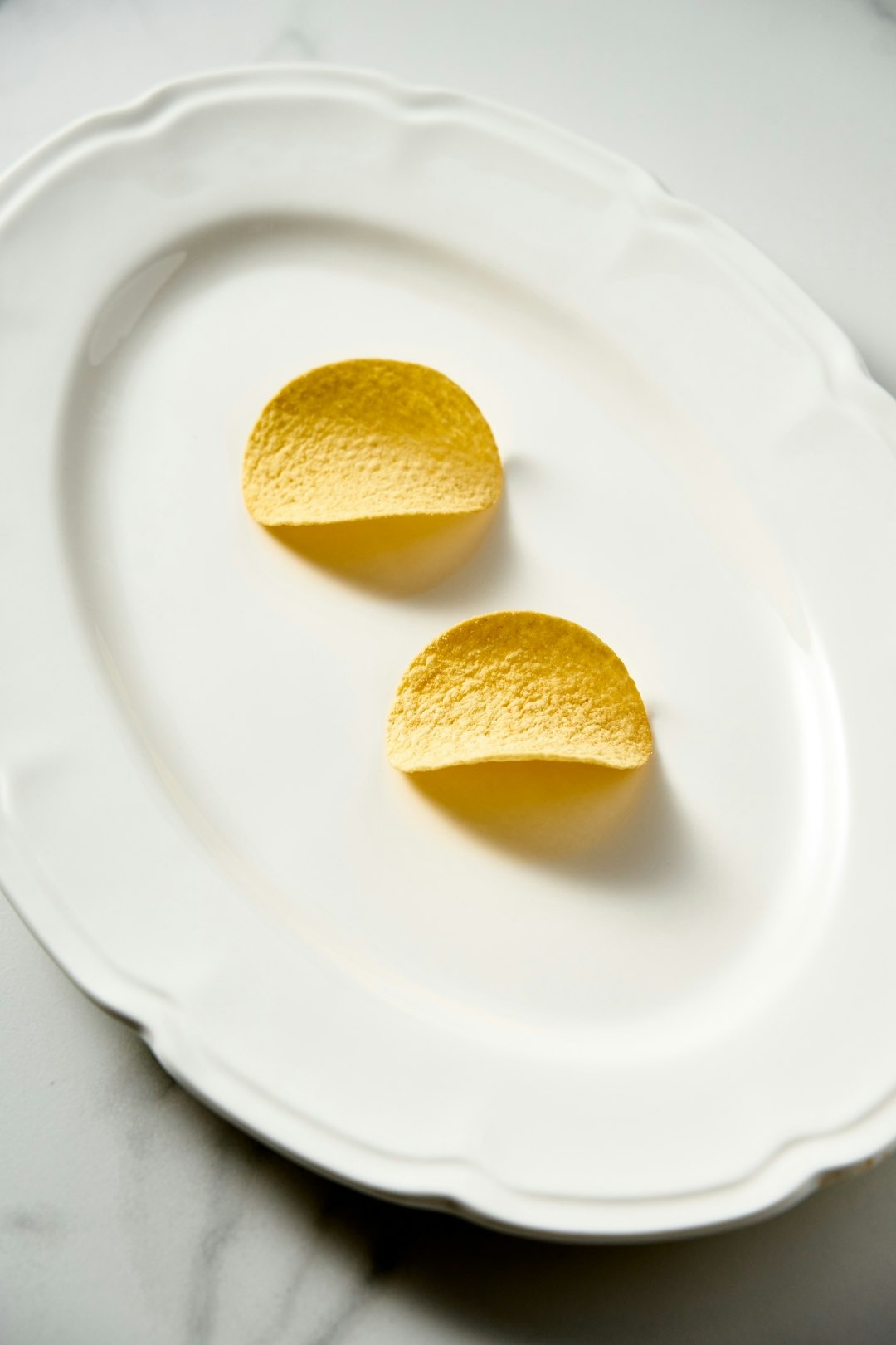 Two golden potato chips rest on a scalloped white platter.